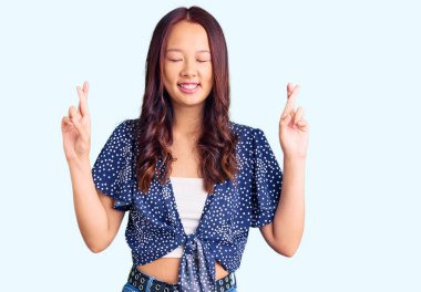 Genç ve güzel Çinli kız günlük kıyafetler giyip umut ve gözlerin kapalı bir şekilde el işareti yaparak gülümsedi. Şans ve batıl inançlar. 