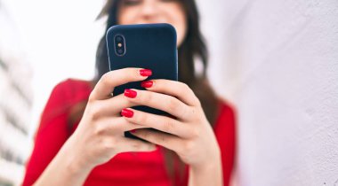 Genç beyaz kadın şehirde akıllı telefon kullanarak mutlu bir şekilde gülümsüyor..