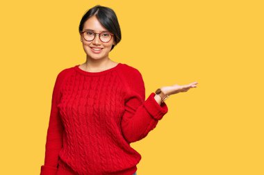 Kısa saçlı, sıradan bir süveter giyen ve gözlüklü, neşeli bir şekilde gülümseyen, avuç içiyle kameraya bakan genç ve güzel İspanyol bir kadın.. 