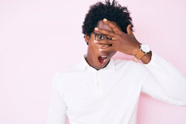 Afro saçlı, iş gömleği ve gözlüklü yakışıklı Afro-Amerikalı adam. Şok olmuş gözlerle yüzünü ve gözlerini kapatıyor, parmaklarından bakıyor. 