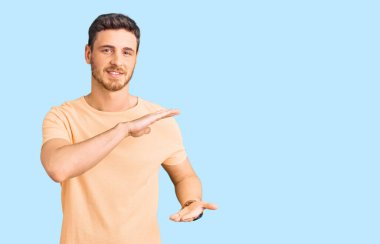 Ayılı yakışıklı genç adam, sıradan sarı tişörtler giyiyor. Elleri büyük ve büyük boy işaretleri gösteriyor. Ölçü sembolü. Kameraya bakıp gülümsüyor. ölçüm kavramı. 