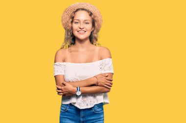 Yazlık şapkalı güzel beyaz kadın kollarını kavuşturup kameraya bakarken gülümsüyor. pozitif kişi. 