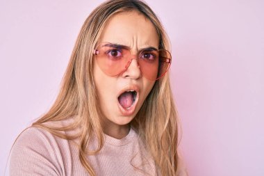 Şok suratlı, kalp şeklinde güneş gözlüğü takan genç, güzel sarışın kadın şüpheci ve alaycı görünüyor. 