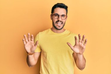 Günlük kıyafetler ve gözlük takan genç İspanyol adam korku ifadesinden korkmuş ve dehşete düşmüş. El kol hareketi yapmayı kes, şok içinde bağır. panik konsepti. 