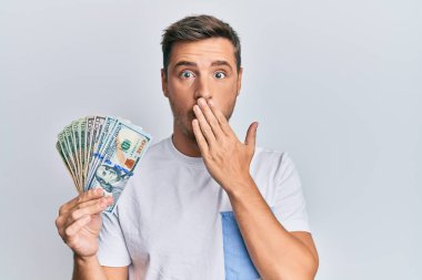 Eli dolarlar tutan yakışıklı beyaz adam, ağzı kapalı, şok olmuş ve hata yapmaktan korkan. şaşırmış ifade 