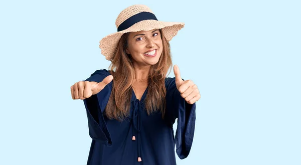 中世のヒスパニック女性は夏の帽子をかぶって手で積極的なジェスチャーを行うことを承認し 親指を上げて笑顔と成功のために幸せ 勝者のジェスチャー — ストック写真