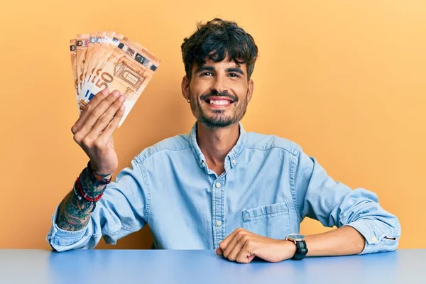 Jovem Hispânico Segurando Notas Euro Sentadas Mesa Parecendo Positivo Feliz — Fotografia de Stock