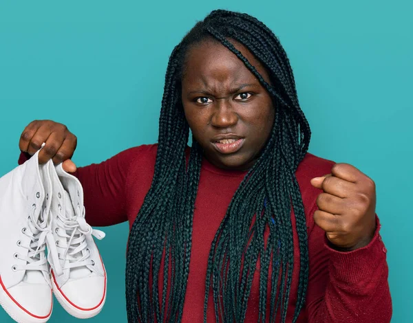 Young black woman with braids holding casual shoes annoyed and frustrated shouting with anger, yelling crazy with anger and hand raised