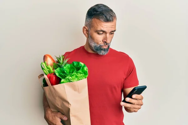 Hombre Guapo Mediana Edad Sosteniendo Bolsa Comestibles Usando Teléfono Inteligente —  Fotos de Stock