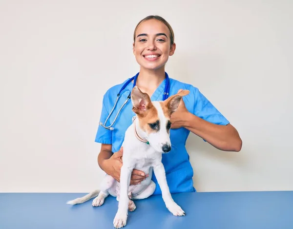 年轻美丽的金发碧眼的兽医女兽医检查狗的健康状况时 面带微笑 面带微笑 大拇指向上做得很出色 并签了字 — 图库照片