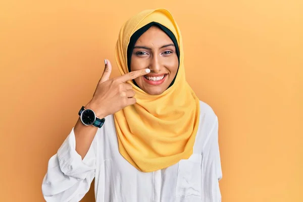 若いブルネットのアラブ女性は 顔と鼻に手の指で指している伝統的なイスラムヒジャーブスカーフを身に着けて 陽気に笑っています 美の概念 — ストック写真