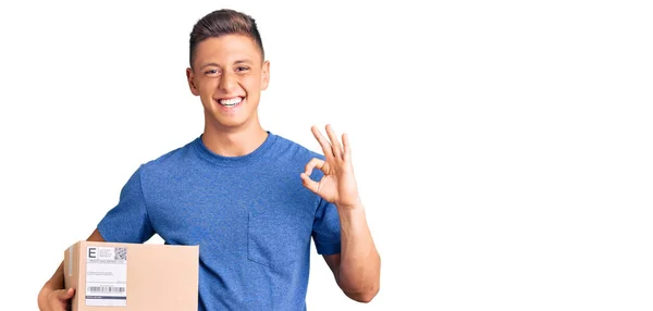 Joven Hombre Hispano Guapo Sosteniendo Paquete Entrega Haciendo Signo Bien — Foto de Stock