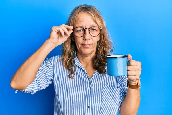 中年金发女人戴着眼镜 喝了一杯咖啡 脸上带着严肃的表情 简单而自然地看着相机 — 图库照片