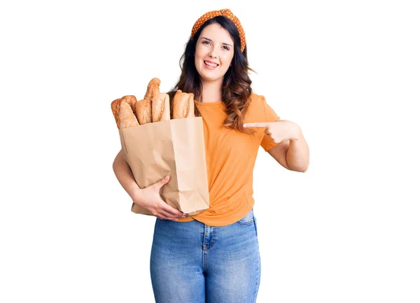 Όμορφη Νεαρή Μελαχρινή Γυναίκα Κρατώντας Χαρτοσακούλα Ψωμί Δείχνοντας Δάχτυλο Έναν — Φωτογραφία Αρχείου