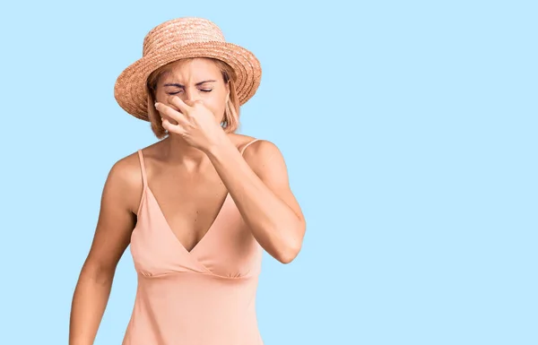 若いブロンドの女性は夏の帽子をかぶって臭いと嫌な匂い 耐えられない匂い 鼻の上に指で息を保持する 臭いが悪い — ストック写真