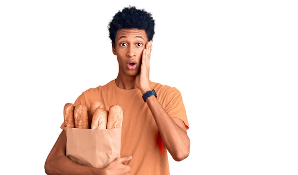 Joven Hombre Afroamericano Sosteniendo Bolsa Papel Con Pan Asustado Sorprendido —  Fotos de Stock