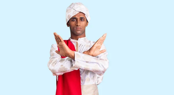 African handsome man wearing tradition sherwani saree clothes rejection expression crossing arms doing negative sign, angry face