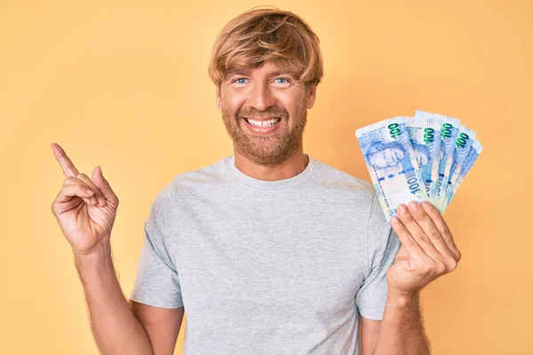 Joven Hombre Rubio Sosteniendo Billetes Rand Sudafricanos Sonriendo Feliz Señalando —  Fotos de Stock
