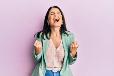 Orta yaşlı esmer kadın gündelik giysiler giyip başarıyı kolları havada ve gözleri kapalı kutluyor. Kazanan konsept. 