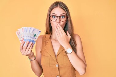 Elinde Kolombiya pezosu tutan genç sarışın kız ağızlarını eliyle kapatıyor, şaşırmış ve hata yapmaktan korkuyor. şaşırmış ifade 