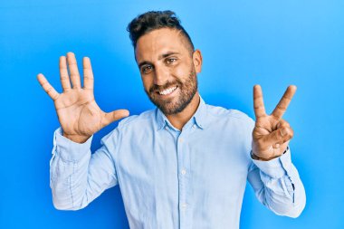 Yakışıklı, sakallı, günlük kıyafetler giyen, 7 numaralı parmaklarıyla gösteriş yapan, kendine güvenen ve mutlu bir adam.. 