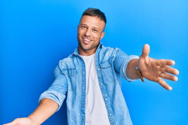 Yakışıklı, sıradan bir kot ceket giyen kaslı adam kameraya bakıp sarılmak için kollarını açmış gülümsüyor. Mutluluğu kucaklayan neşeli bir ifade.. 