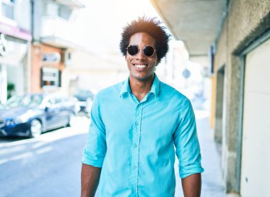 Genç, yakışıklı, Afro-Amerikan bir adam. Günlük kıyafetler ve güneş gözlüğü takıyor. Mutlu gülümsüyor. Yüzünde gülümsemeyle kasaba caddesinde yürürken.
