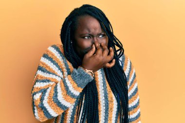 Örgülü, sıradan bir kazak giyen genç siyahi bir kadın pis ve iğrenç bir koku alıyor. Nefesini burnunda tutuyor. Kötü kokuyor. 