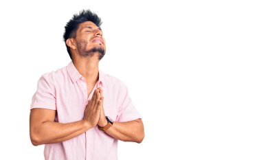 Yakışıklı Latin Amerikalı genç adam, sıradan bir yaz gömleği giyiyor. Elleriyle yalvarıyor ve dua ediyor. Yüzünde umut ifadesi var. Yalvarıyor. 