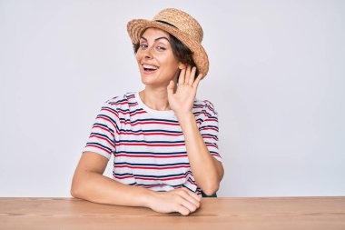 Gündelik giysiler ve şapka giymiş genç İspanyol bir kadın masaya oturmuş, sırıtarak dedikodu ya da dedikoduları dinliyor. Sağırlık kavramı. 