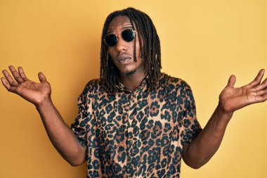 Saç örgülü, hayvan desenli tişörtlü ve güneş gözlüklü Afro-Amerikan bir adam. Hiçbir fikrim yok ve şüpheli bir yüzüm var.. 