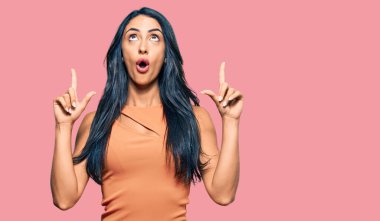 Yazlık elbise giyen güzel İspanyol kadın şaşırmış ve şaşırmış bir şekilde yukarı bakıyor ve parmaklarıyla işaret ediyor ve kollarını kaldırıyor.. 