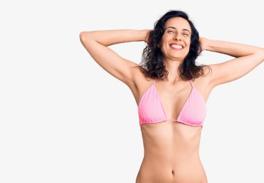 Genç ve güzel İspanyol kadın bikini giyiyor, rahatlıyor ve esniyor, kolları ve elleri başının ve boynunun arkasında mutlu bir şekilde gülümsüyor. 