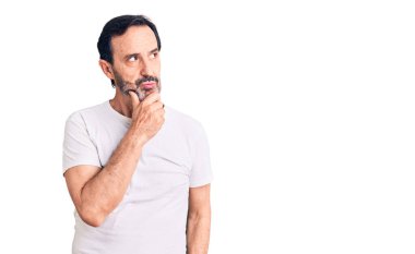 Orta yaşlı yakışıklı bir adam, elleri çenesinde gündelik tişörtler giyip soru soruyor, düşünceli bir yüz ifadesi var. Düşünceli bir yüzle gülümsüyor. şüphe kavramı. 