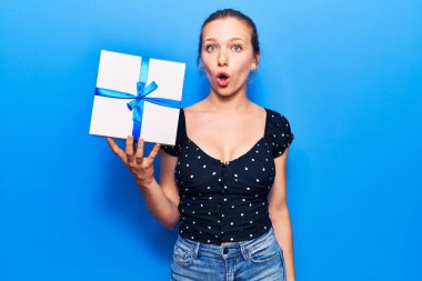 Elinde hediye tutan genç sarışın kadın korkmuş ve ağzı açık hayret içinde şaşkınlık içinde, inançsız bir yüz. 