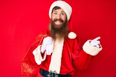 Uzun sakallı, yakışıklı, Noel Baba kostümü giyen ve gülümseyen, mutlu, eli ve parmağı yanda olan genç bir adam. 