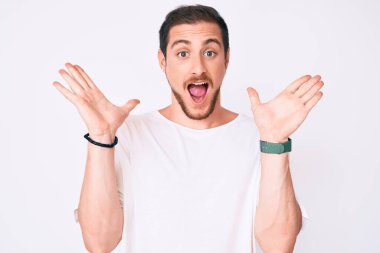 Sıradan beyaz tişörtler giyen genç yakışıklı adam çılgın ve başarıyı kollarını kaldırıp heyecanla haykırarak kutluyor. Kazanan konsept 