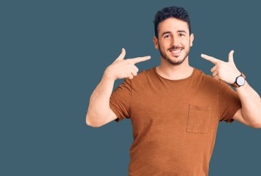 Günlük kıyafetler giyen, neşeli gülümseyen, parmaklarıyla ve ağzıyla işaret eden İspanyol genç bir adam. diş sağlığı kavramı. 