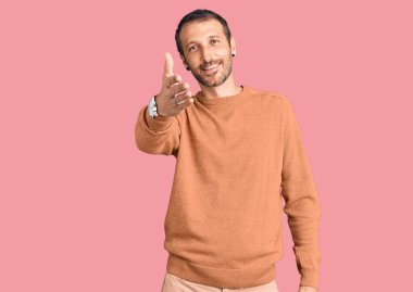 Gündelik kıyafetler giyen genç yakışıklı adam dostça bir selamlama ve hoş geldin hediyesi olarak el sıkışmayı sunuyor. başarılı iş. 