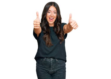 Güzel, esmer, siyah gömlekli genç bir kadın. Elleriyle olumlu bir jest yapıyor. Gülümsüyor ve başarı için seviniyor. kazanan jest. 