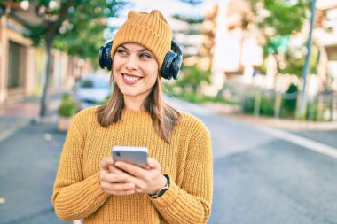 Şehirde akıllı telefon ve kulaklık kullanan genç sarışın kadın..