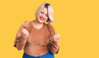 Genç sarışın ve cüsseli bir kadın gündelik süveter giyiyor. Çok mutlu ve heyecanlı. Kolları havada, gülümseyen ve başarı için çığlık atan kazanan bir jest yapıyor. kutlama konsepti. 