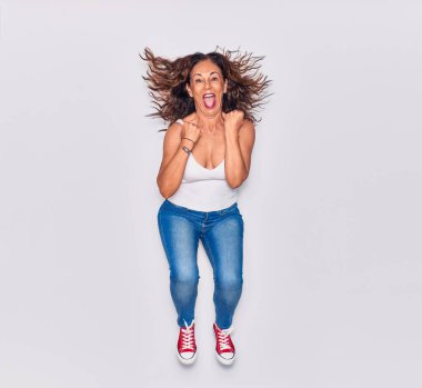 Orta yaşlı, güzel, İspanyol bir kadın. Günlük kıyafetler giyip mutlu gülümsüyor. Yüzünde tebessümle zıpla kazanan jest yap yumruklarını yalıtılmış beyaz arka planda tut