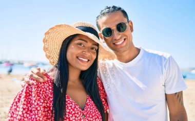 Genç Latin çift, mutlu bir şekilde gülümsüyor ve sahilde sarılıyorlar..
