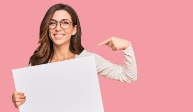 Boş afiş taşıyan genç esmer kadın mutlu ve gururlu bir kendini işaret ediyor. 