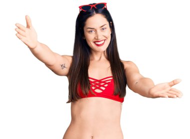 Bikini giyen beyaz bir kadın kameraya sarılıp gülümseyerek gülümsüyor. Mutluluğu kucaklayan neşeli bir ifade.. 