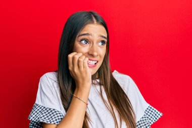 Günlük kıyafetler giyen genç İspanyol kadın gergin ve gergin görünüyor. Ağzı tırnak yiyen ellerle. anksiyete. 