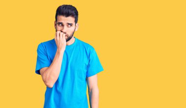 Sakallı, sıradan tişörtlü, stresli ve gergin görünen dudakları tırnak yiyen genç yakışıklı bir adam. anksiyete. 