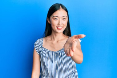 Sıradan çizgili tişört giyen genç Çinli bir kadın dostça el sıkışarak selamlama ve hoş geldin diyor. başarılı iş. 