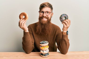 Genç İrlandalı kızıl adam kahvaltıda çörek yerken yüzünde mutlu ve havalı bir gülümsemeyle gülümsüyor. diş gösterme. 